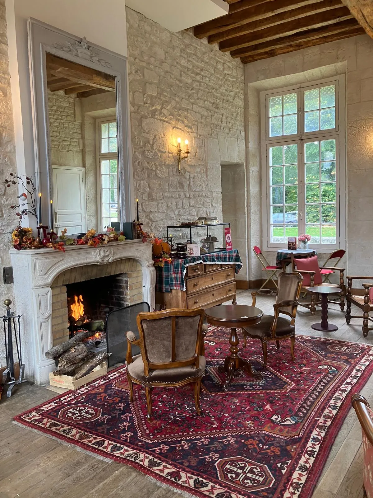 La salle du salon de thé : cheminée allumée, tapis, fauteuils et tables